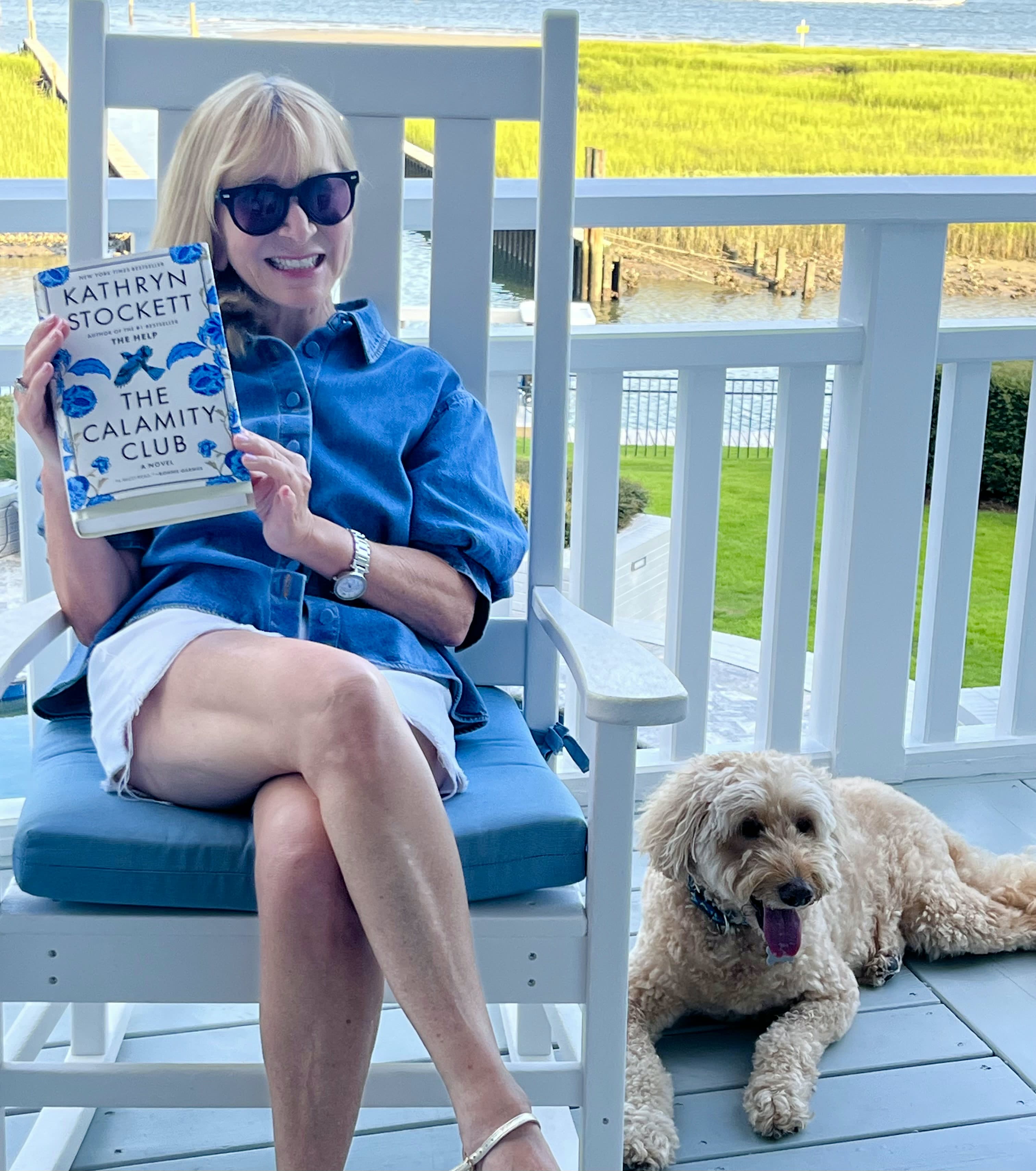 Mindy reading The Calamity Club with her Labradoodle on a coastal porch