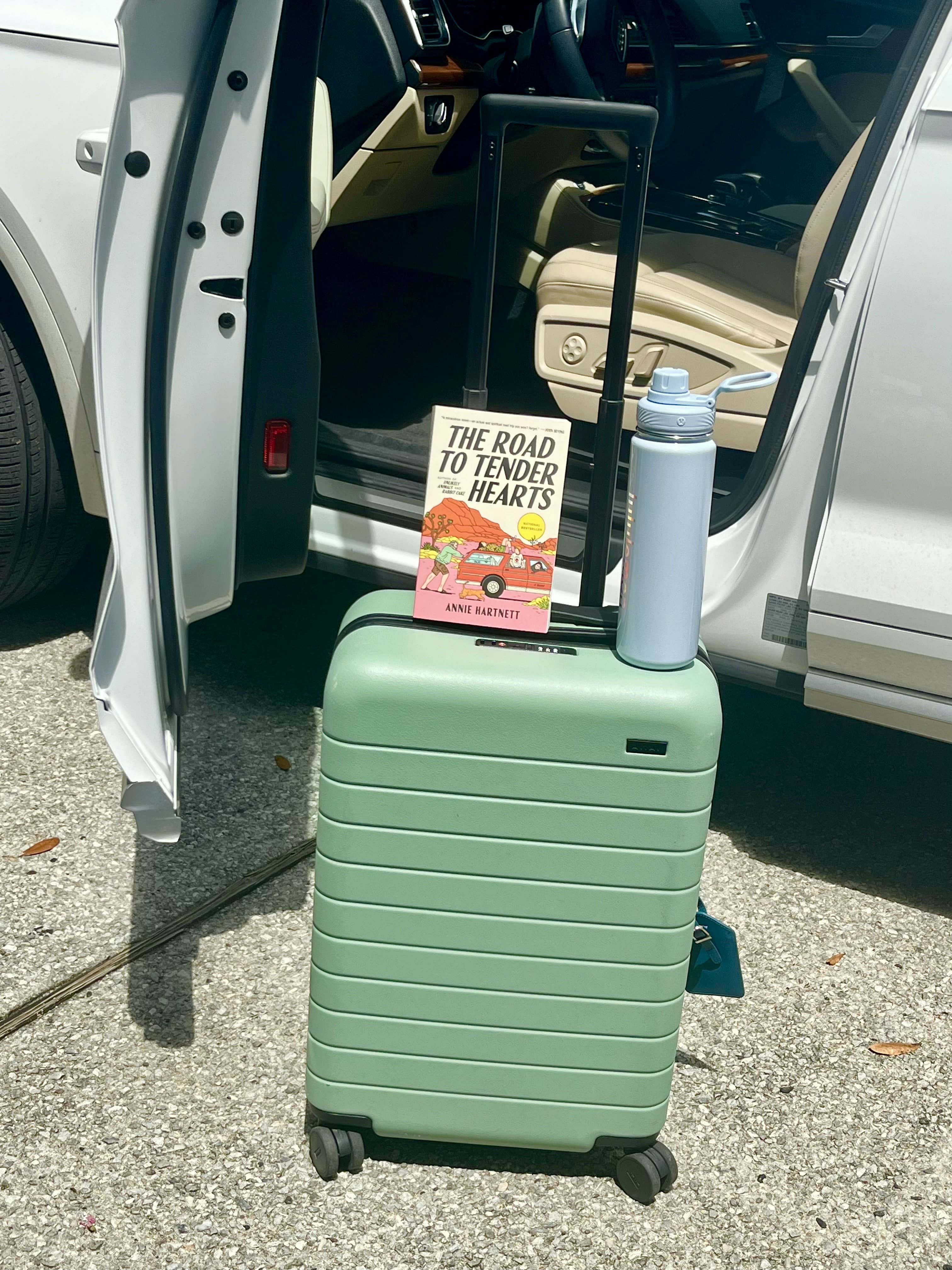 The Road to Tender Hearts packed beside a green suitcase and travel mug