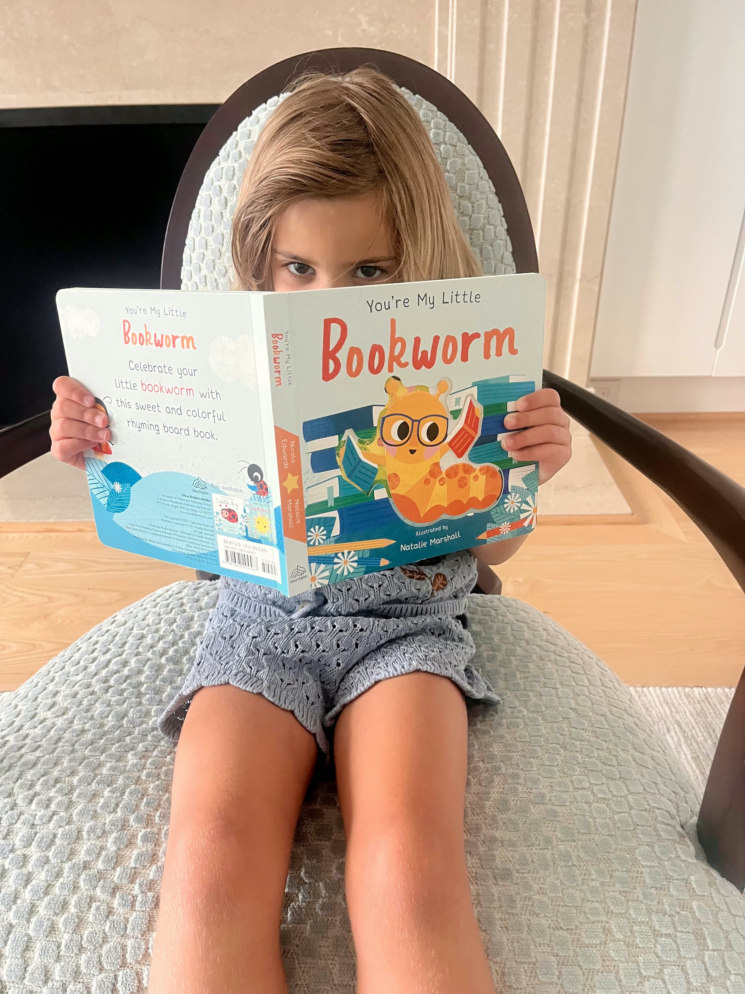 A young child reading My Little Bookworm in a cozy chair